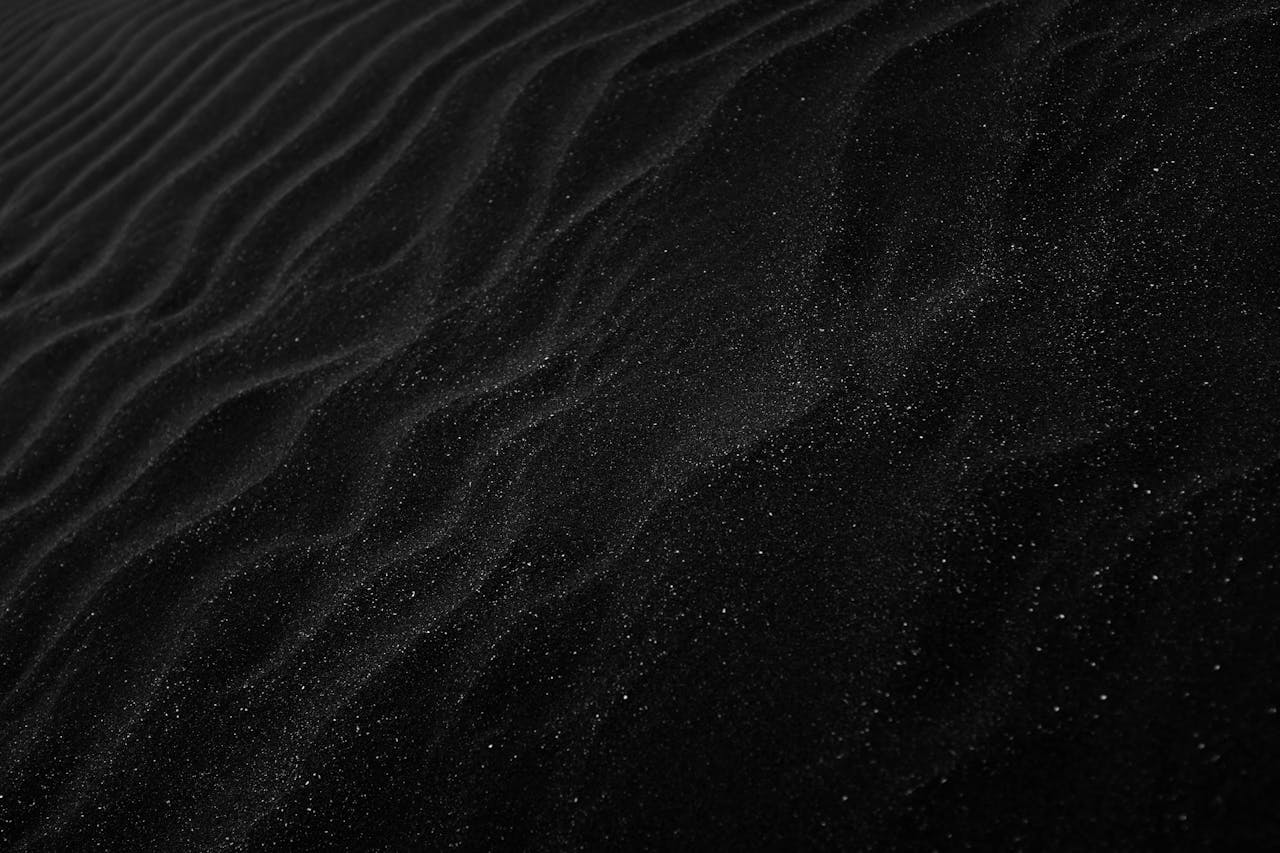 Home Textured black sand with ripples resembling dunes, creating a dark, abstract aesthetic.