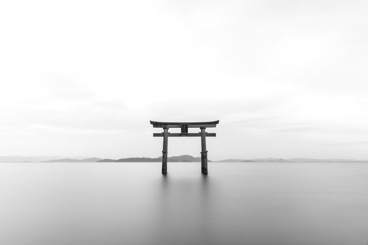 Home Serene black and white image of a torii gate standing in calm waters, symbolizing tranquility.