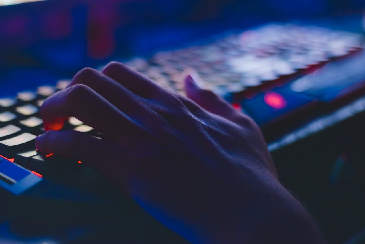 Home A hand typing on a glowing keyboard in dim lighting, perfect for tech themes.